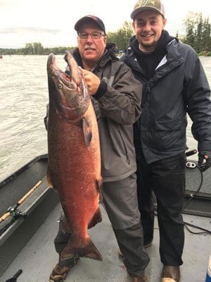 two men holding large salmon on fishing boat