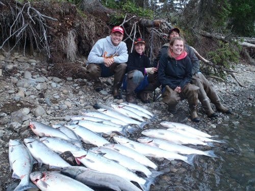 men and woman smiling next to two rows of salmon