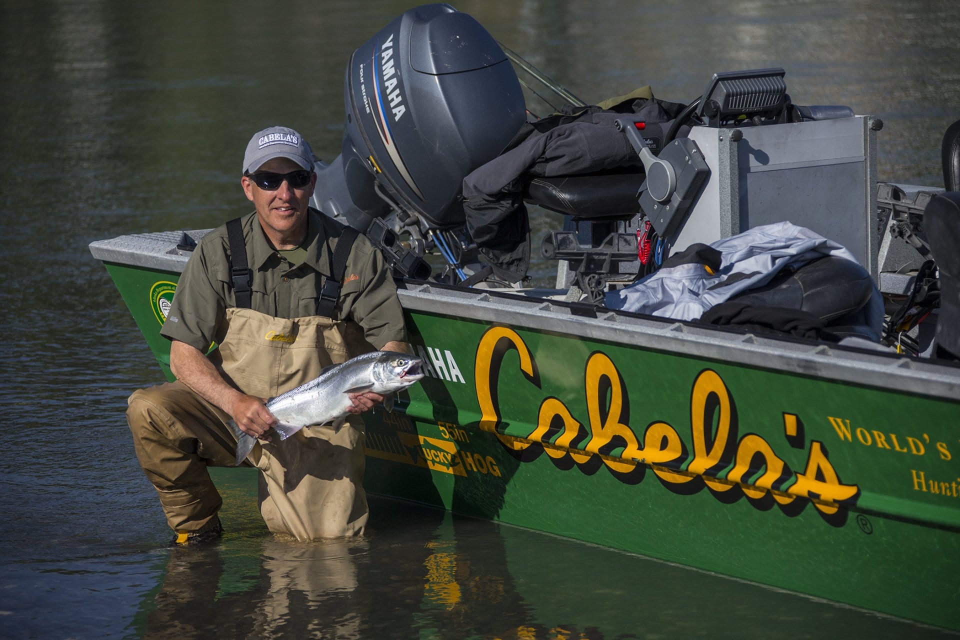 man in hip waders holding fish in front of boat