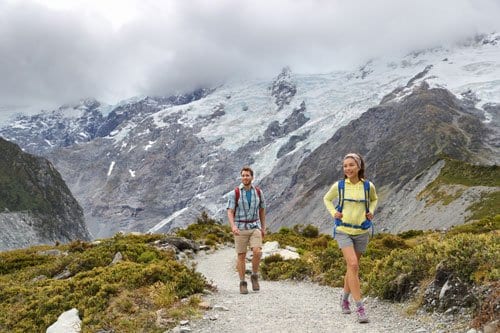 Male and female hiker in casual summer gear walking up a gravel path in the mountains on a cloudy day