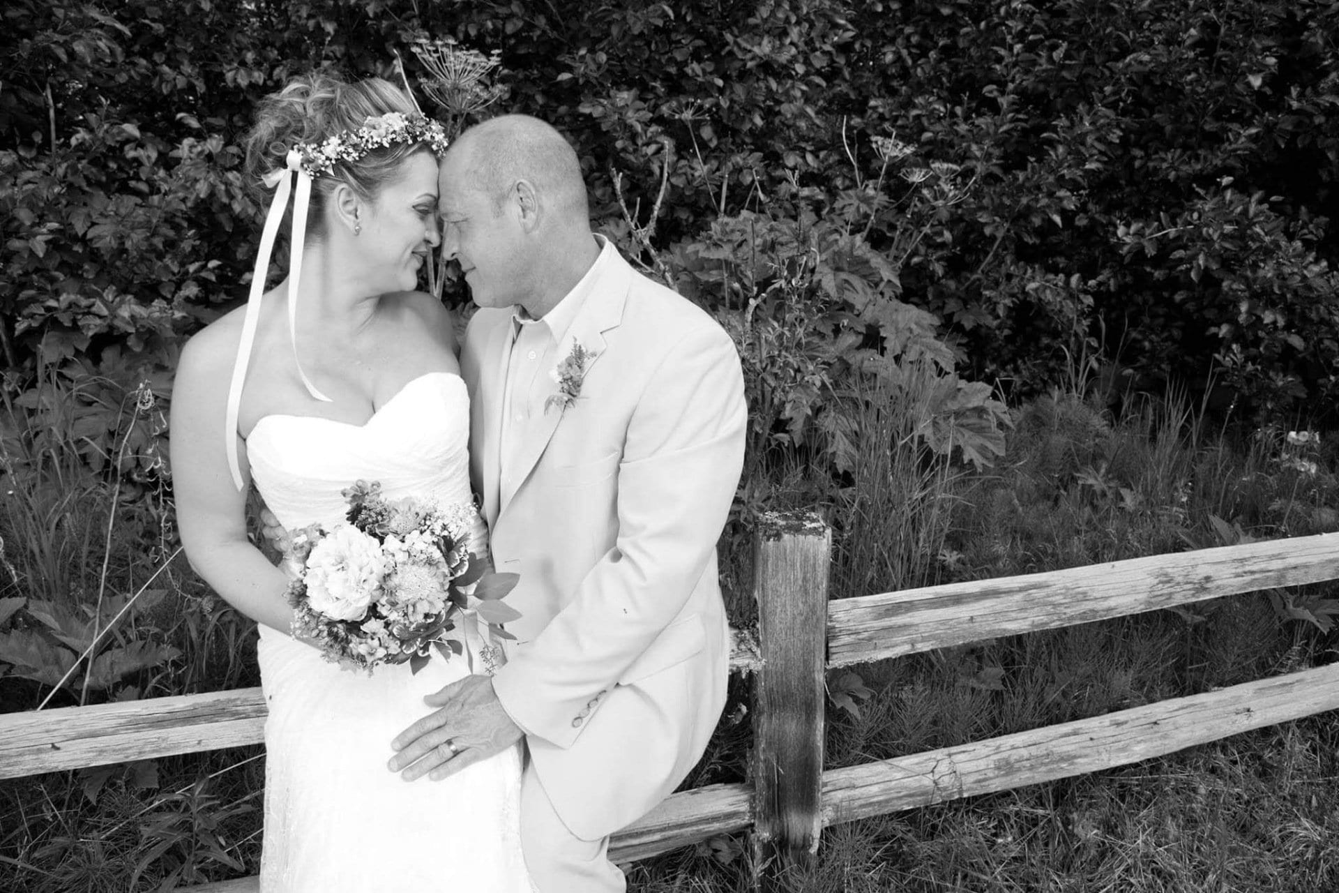 Black and white image of a newlywed couple flirting while sitting together on a rustic fence