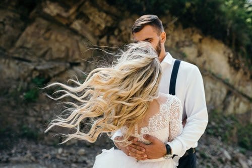 Blonde wavy-haired bride embracing bearded groom in suspenders