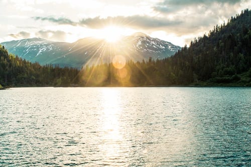 sun shining over mountain onto lake