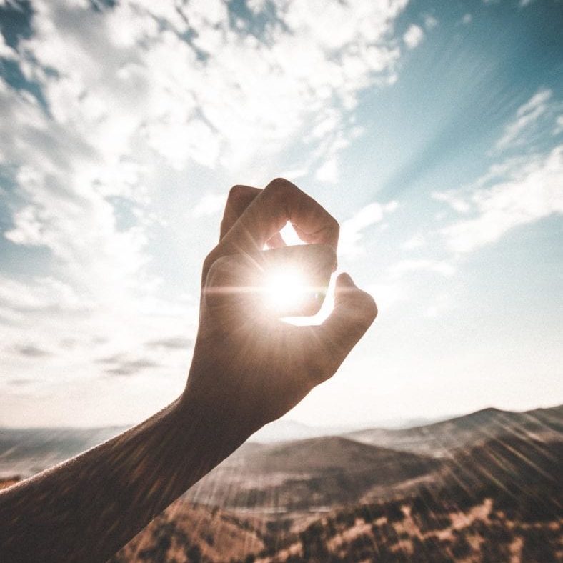 hand making shape in front of sun