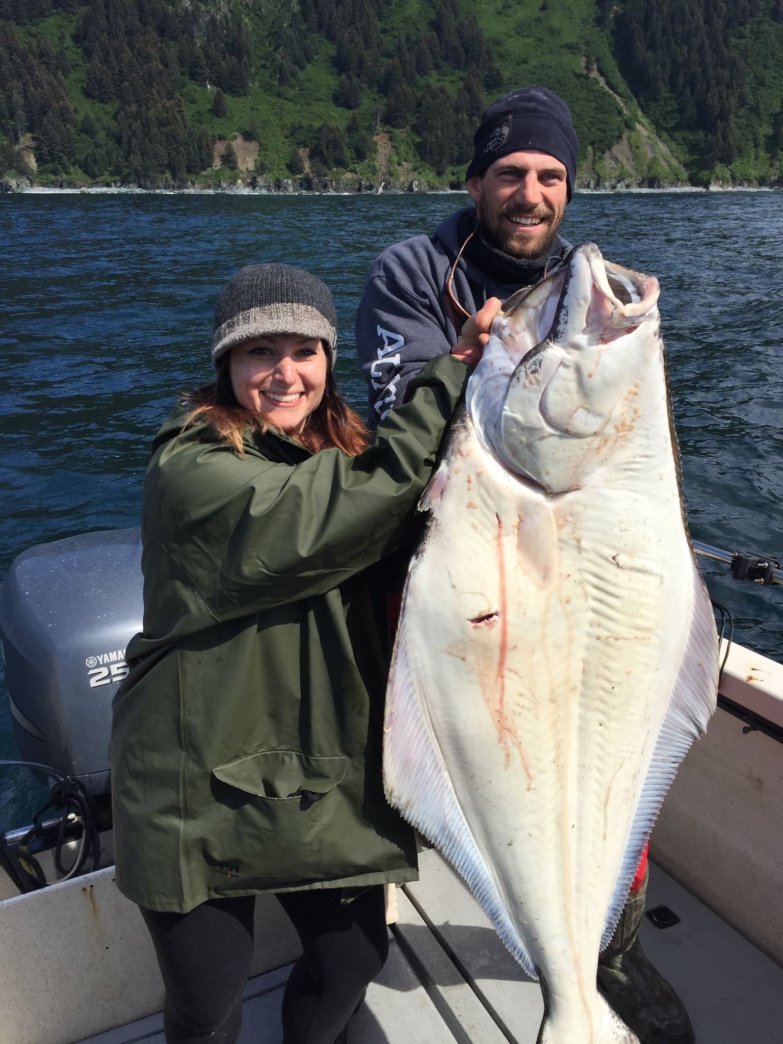 a couple standing on a boat showing off a big alaskan halibut they caught