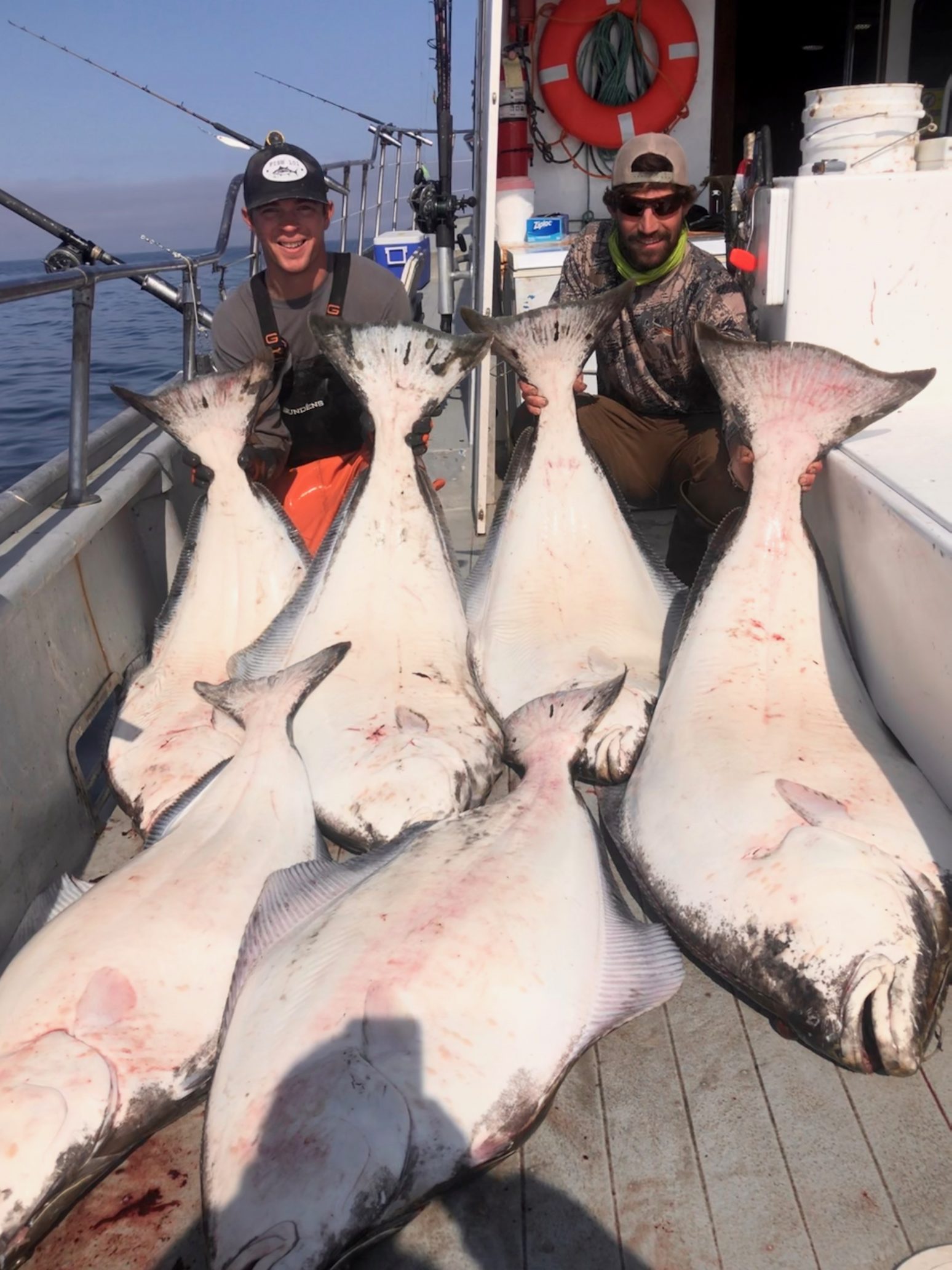 two men on a boat with 6 large halibut they caught in alaska