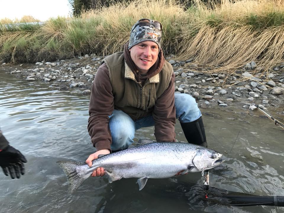 man croughing in a river infront of his prize salmon