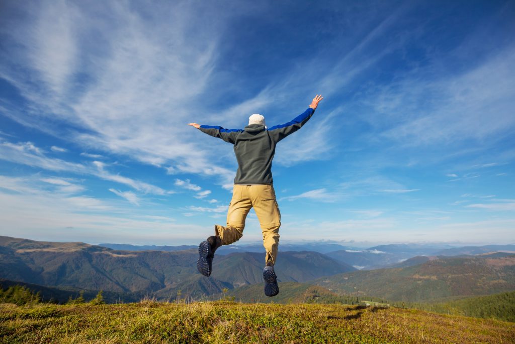 happy man jumping in front of mountains and blue sky with spread arms