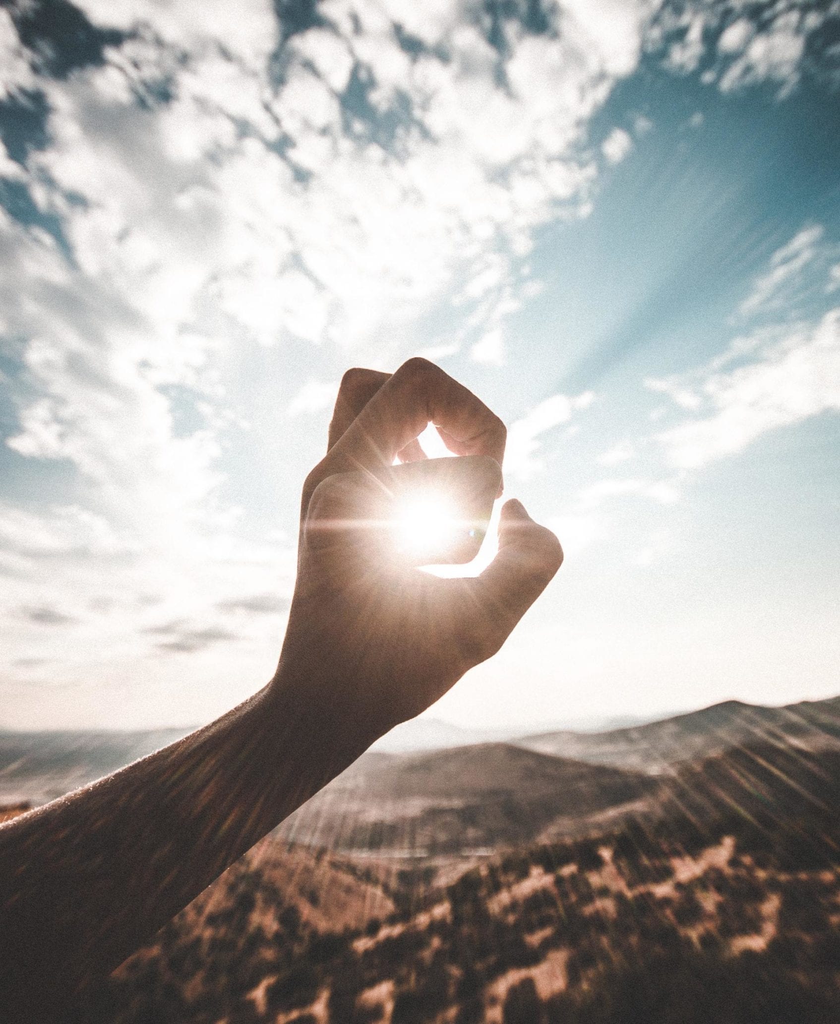 hand making shape in front of sun