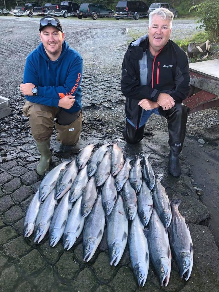 two men kneeling in front of a mountain of fish